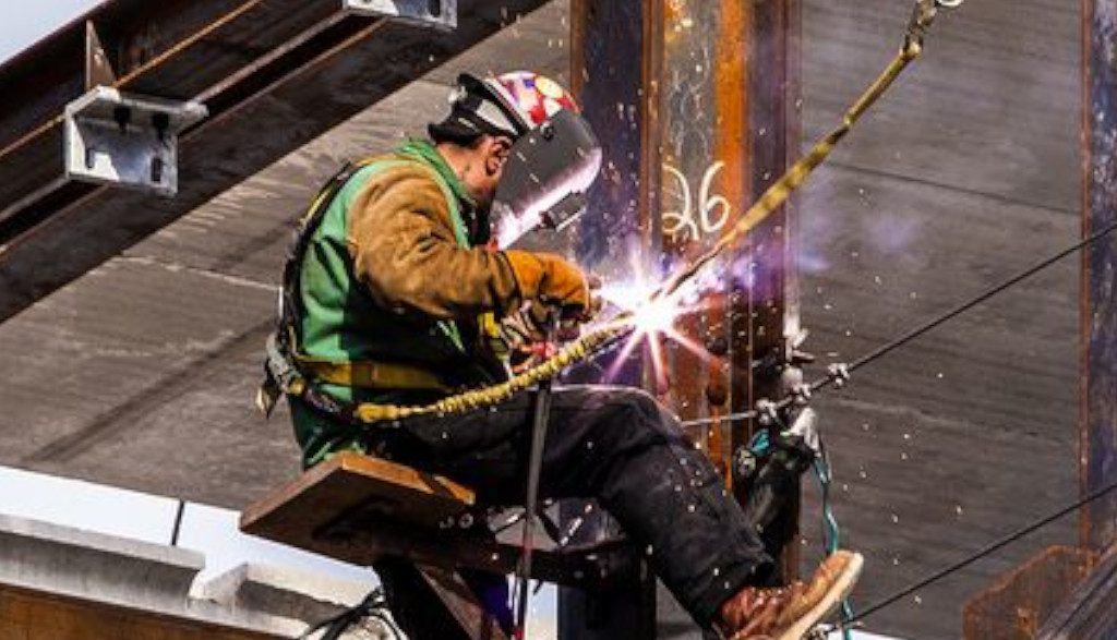 A man welding on top of a metal pole.